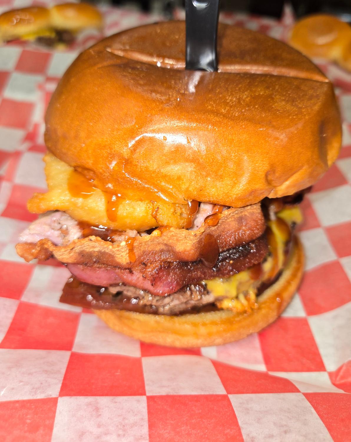 BBQ burger with bacon, a fried onion ring and smoked meat on a brioche bun